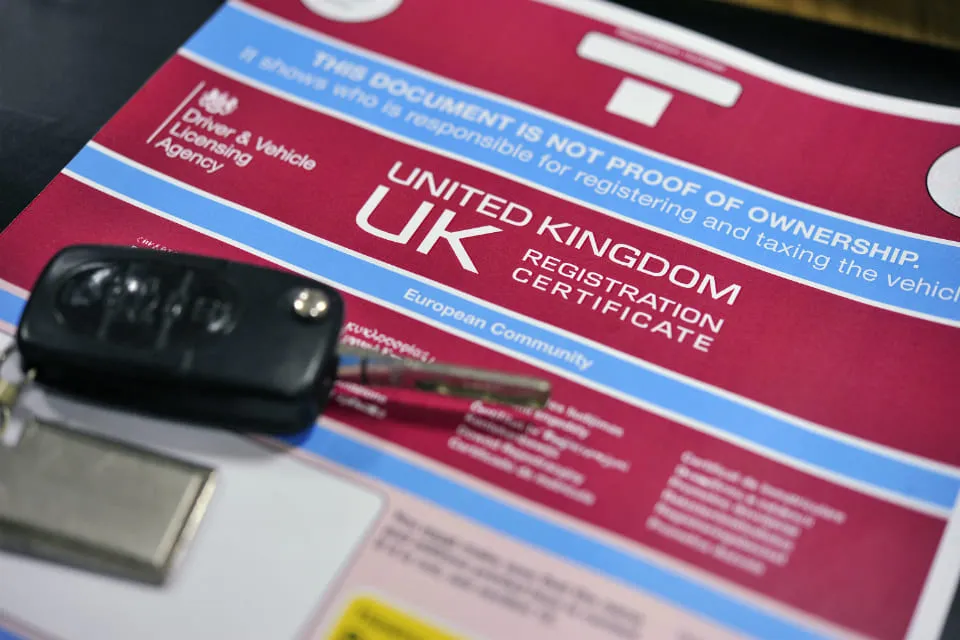 A red UK V5C vehicle registration certificate with a set of car keys resting on it.
